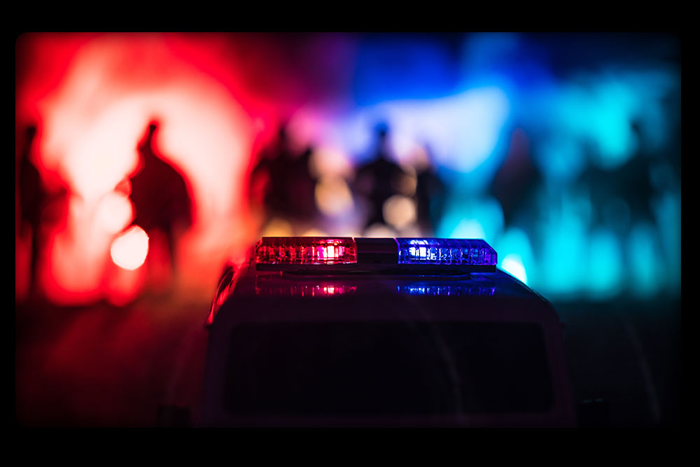 Blurred image of crowd assembled at night with police lights in foreground